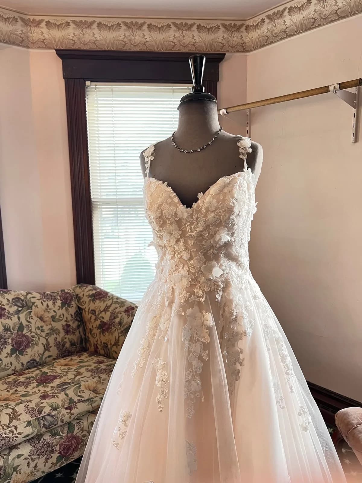 A white lace wedding gown on a mannequin in the shop's front room, by the window