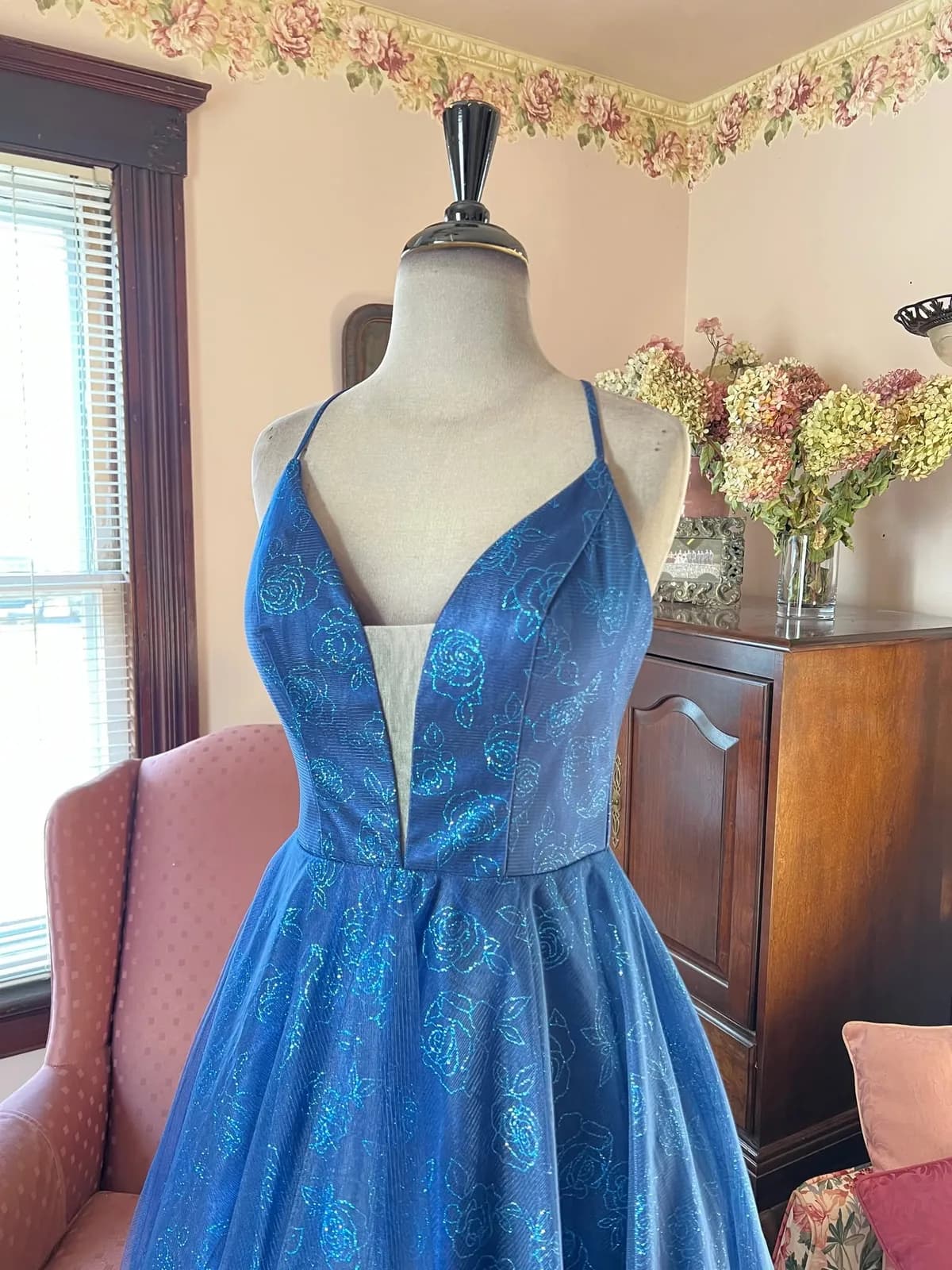 A royal blue sparkle ball gown on a mannequin beside the shop's pink armchair