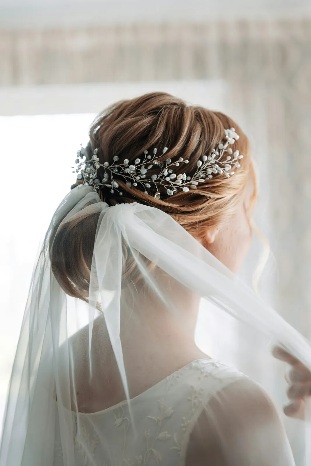 A bride wearing a crystal headpiece and a long veil, seen from behind